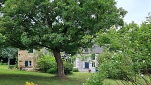 Una casa in pietra con un giardino, un albero grande e un aiuola di fiori.