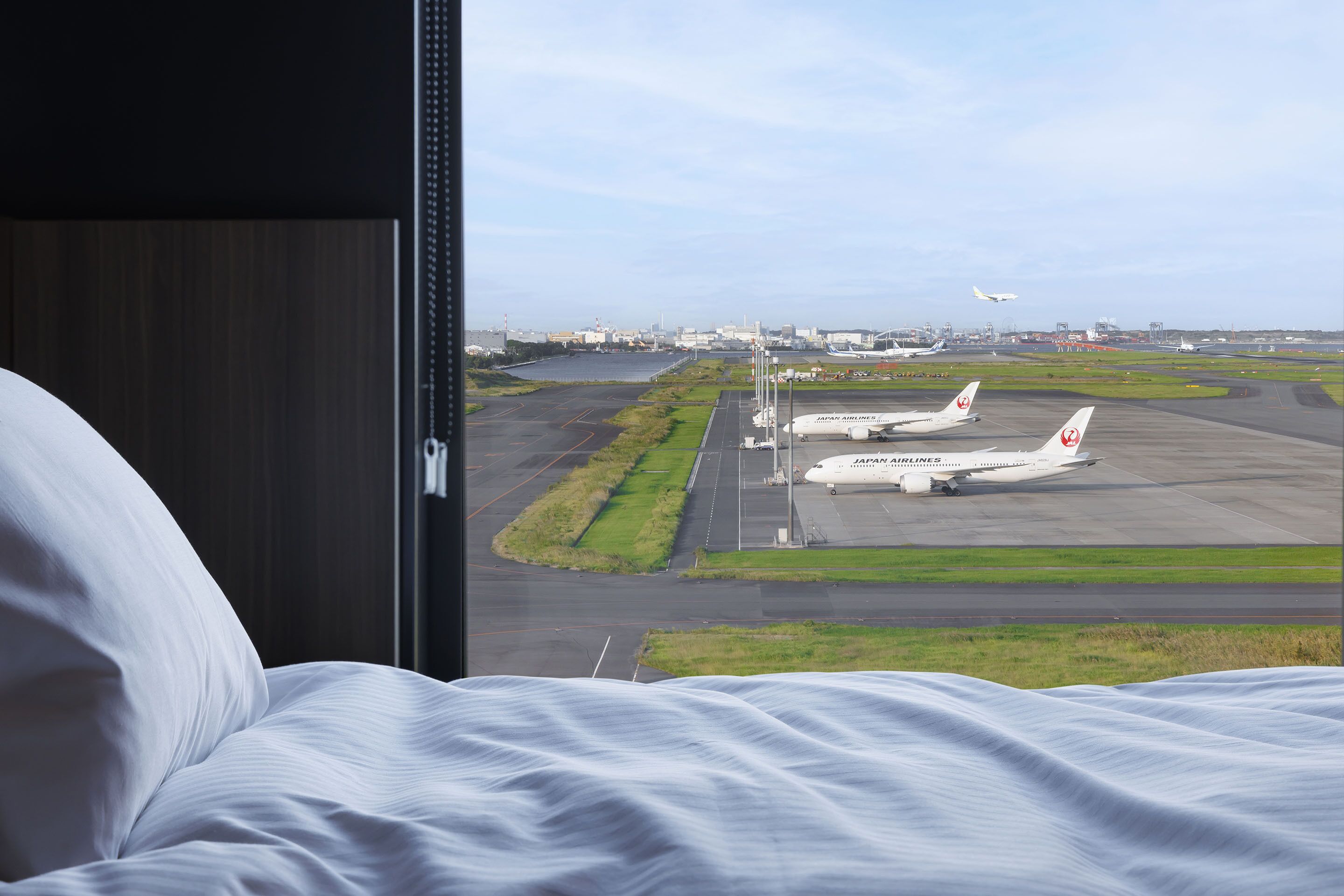 A hotel room with a view of an airport, including a Japan Airlines airplane on the tarmac.