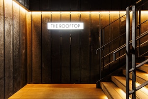 Una escalera con un letrero que dice "THE ROOFTOP" que lleva a una zona con piso de madera.