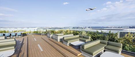 Terraço no telhado com área de estar externa, vista da cidade e um avião no céu.