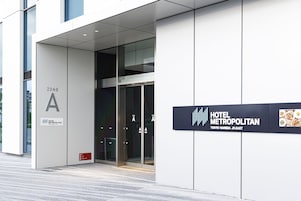 Una entrada de hotel moderna con puerta de vidrio, un letrero que indica 'HOTEL METROPOLITAN TOKYO HANEDA JR-EAST' y un cartel que dice 'ZONA A'.