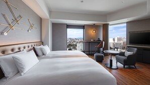 Une chambre d’hôtel moderne avec deux lits, un coin salon, une télévision et une vue sur la ville.