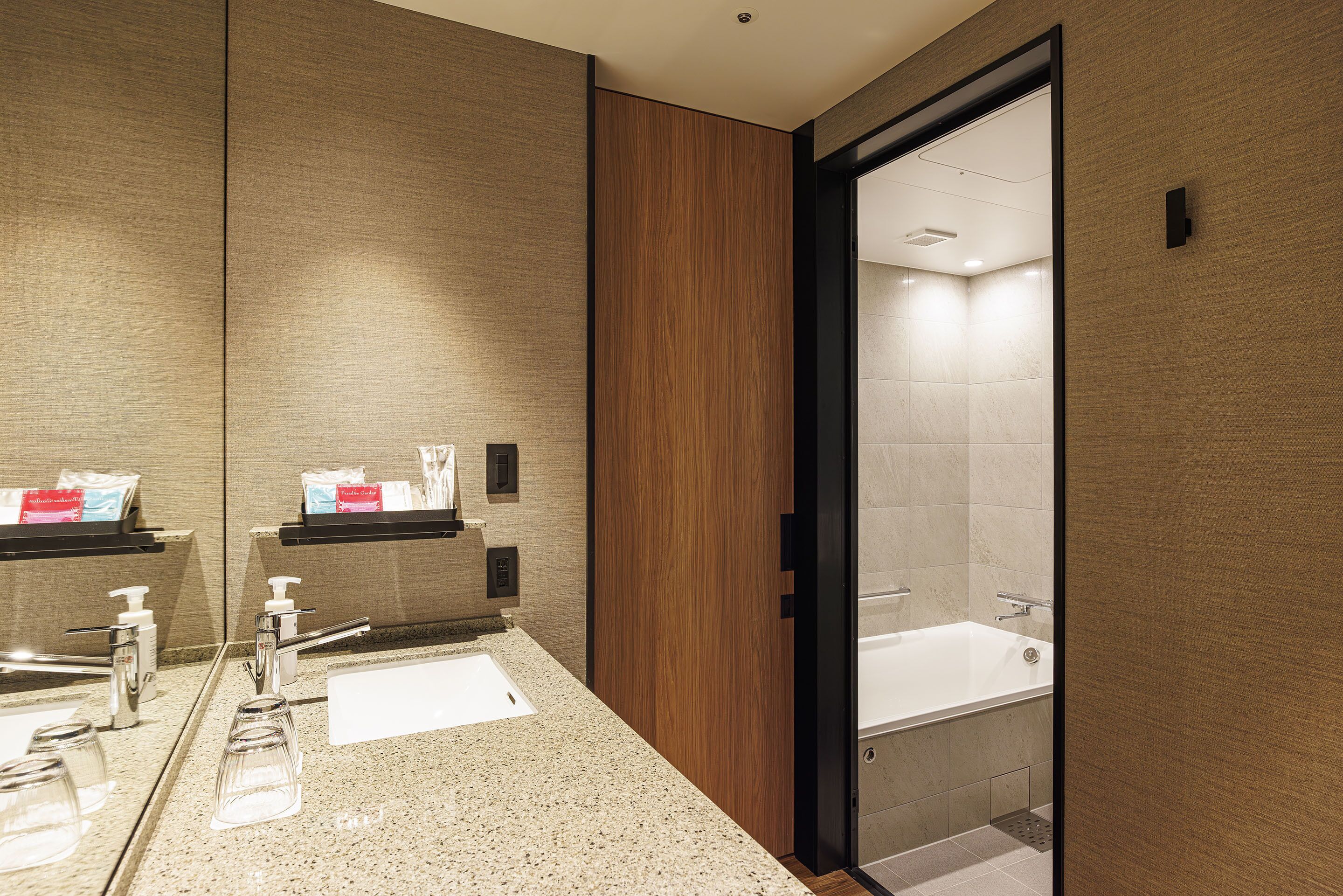 A modern bathroom with a large mirror, two sinks, a bathtub, and a wooden panel on the wall.