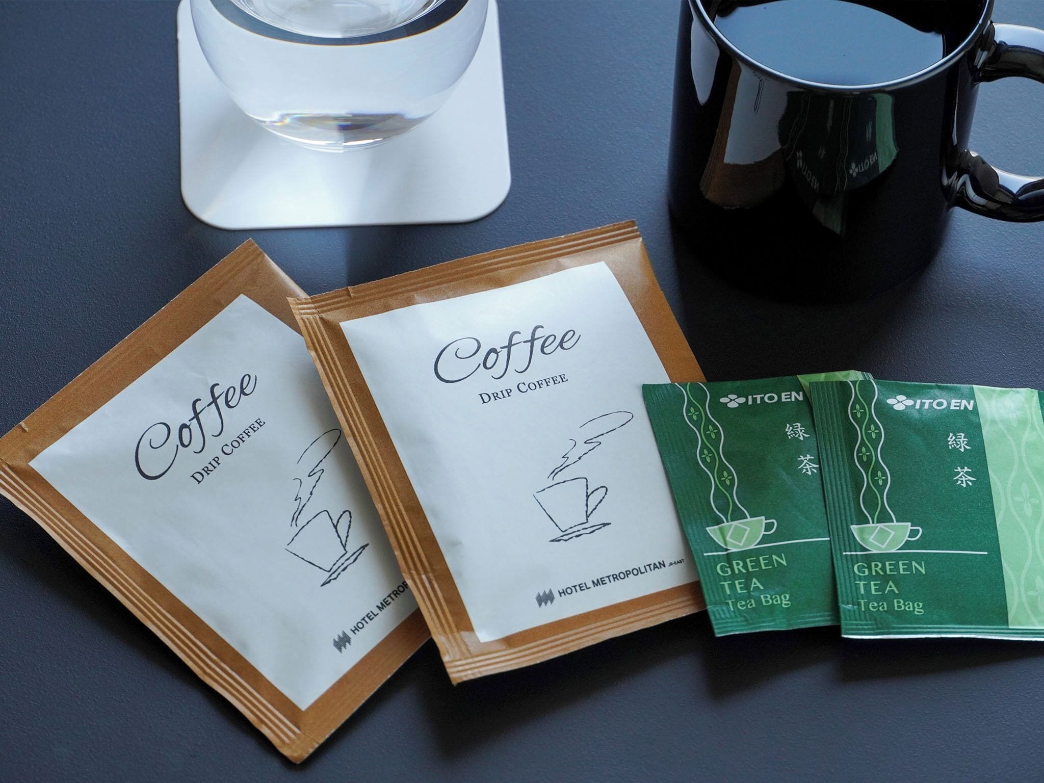 Two coffee bags, a glass of water, and a black mug on a table.