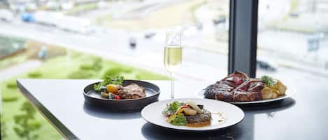 Une table avec deux assiettes de nourriture et un verre de vin, donnant sur un paysage urbain avec des immeubles et une autoroute.