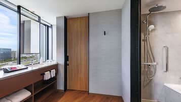 A modern bathroom with a shower, a vanity with a mirror, and a view of the city.