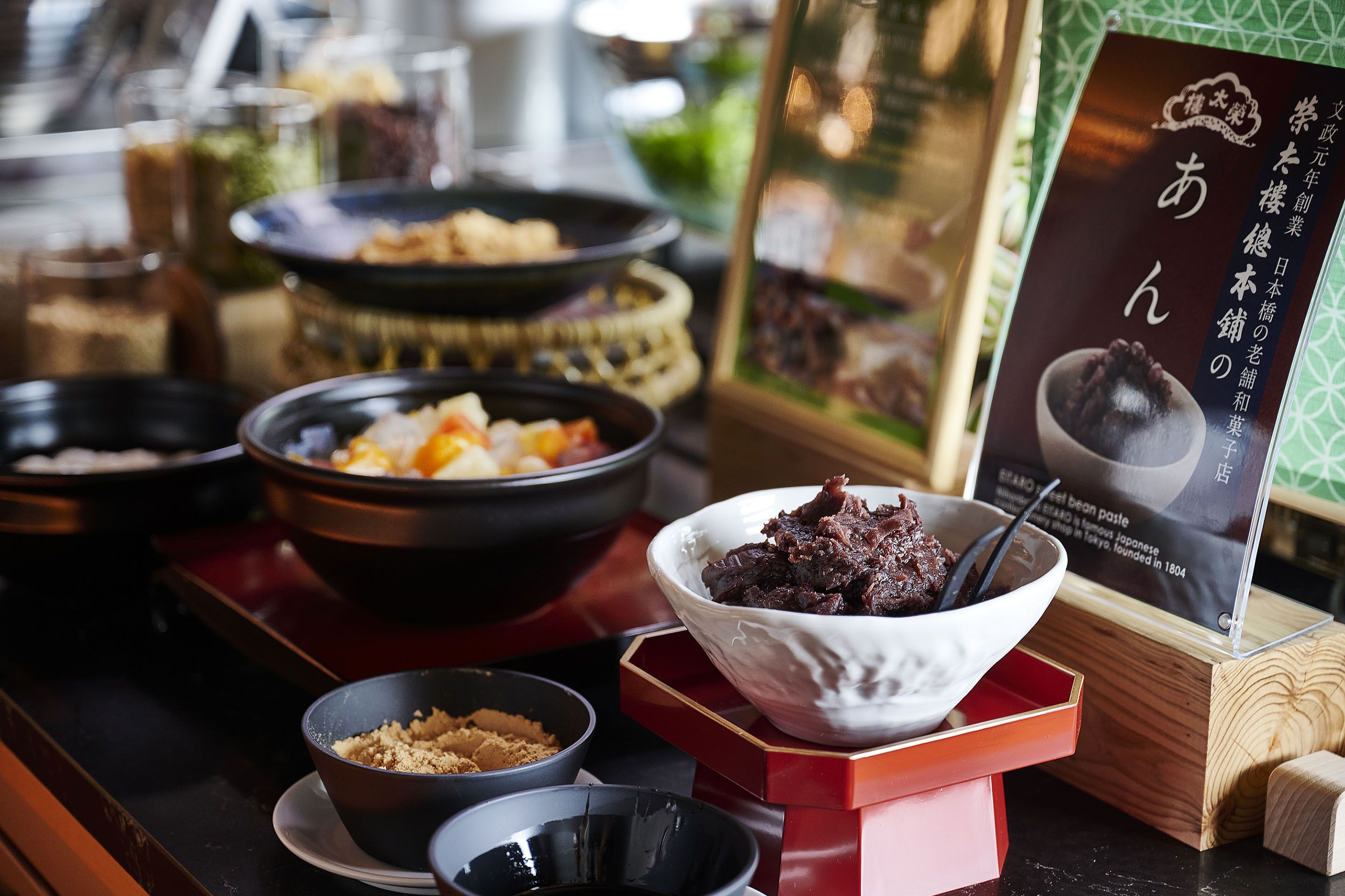 A variety of dishes on a buffet table, including a bowl of what appears to be a bean paste dish, a bowl of rice, and other assorted foods.