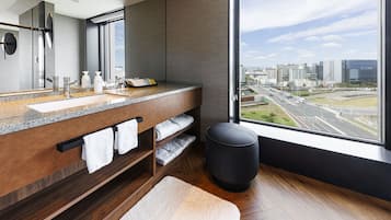 Une salle de bain moderne dotée d’un grand miroir, d’un comptoir en granit et offrant une vue sur la ville grâce à de grandes fenêtres.