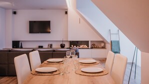 A dining area with a wooden table set for four, surrounded by white chairs. A television is mounted on the wall above the dining area. - Modern apartment in the center of Nieuwpoort (Nieuwpoort)