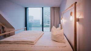 A modern bedroom with a large bed, a view of a cityscape through a large window, and a unique wall-mounted light fixture. - Modern apartment in the center of Nieuwpoort (Nieuwpoort)