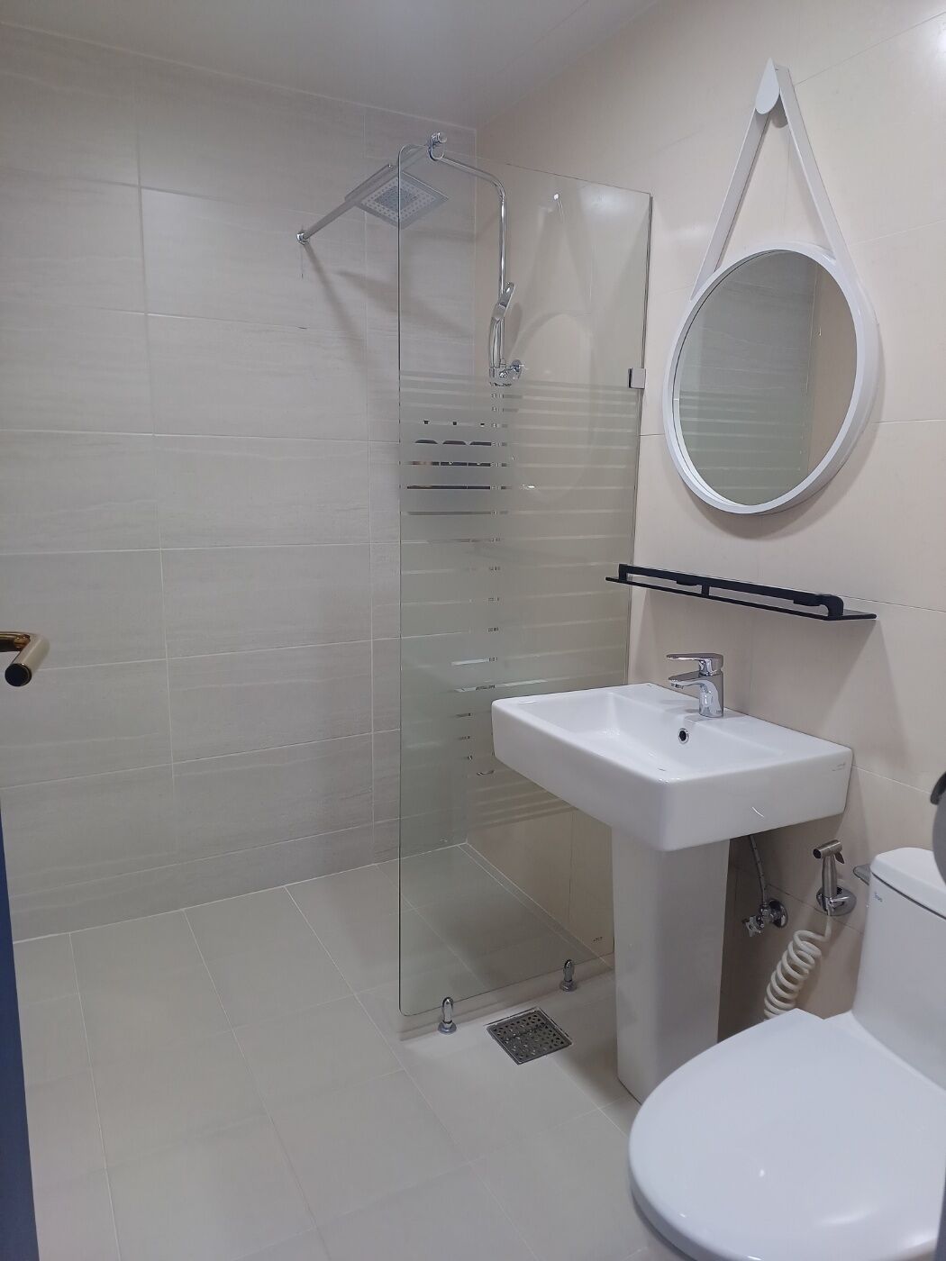 Ein Badezimmer mit einer Duschkabine aus Glas, einem weißen Waschbecken, einer Toilette und einem runden Spiegel an der Wand.