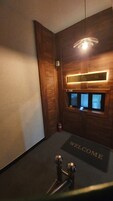 Uma área de recepção de hotel com um balcão de madeira, um tapete de boas-vindas e um extintor de incêndio.