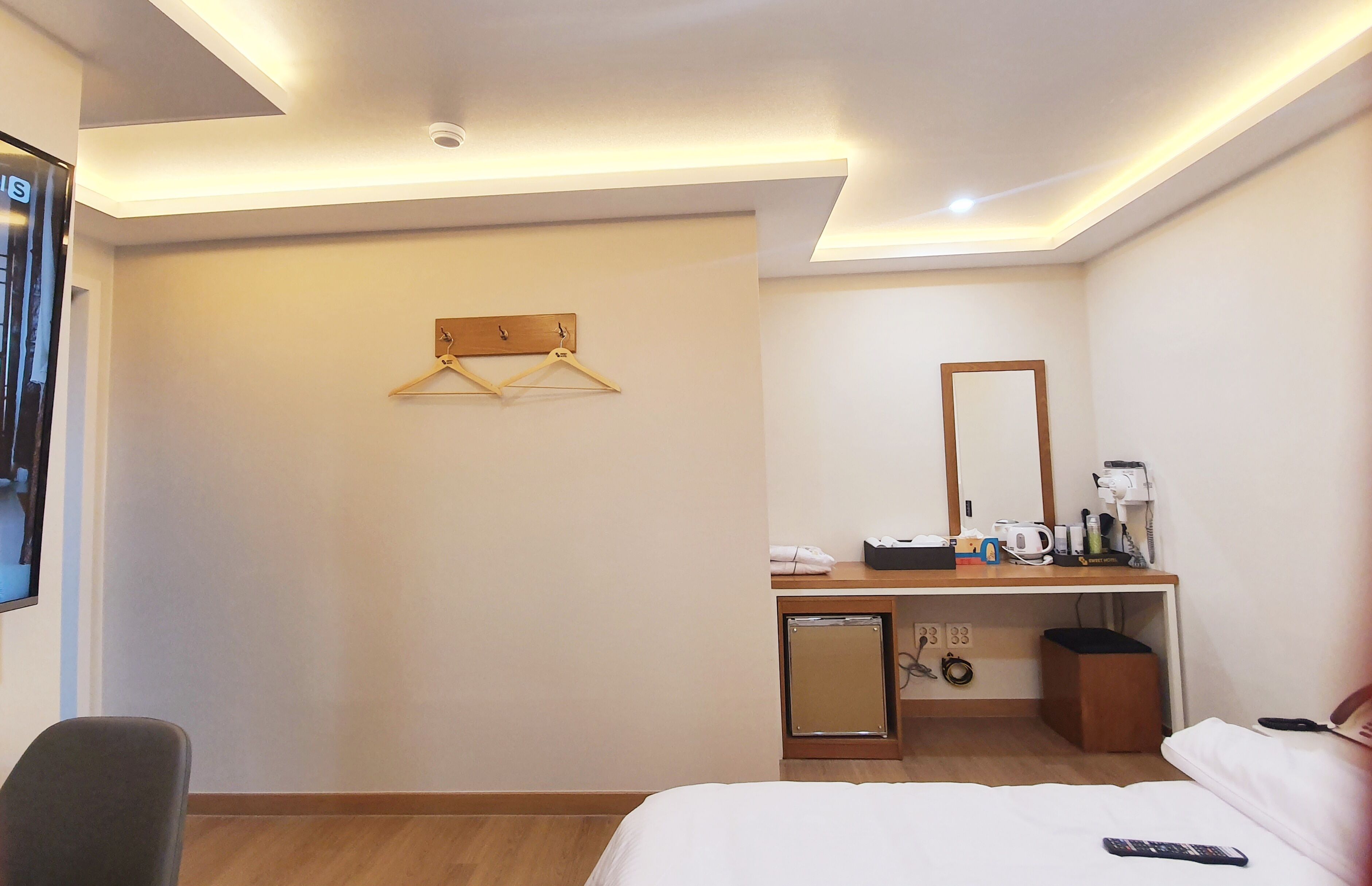 A hotel room with a bed, a desk with a mirror, a hanging clothes rack, and a small cabinet.