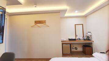 A hotel room with a bed, a desk with a mirror, a hanging clothes rack, and a small cabinet.