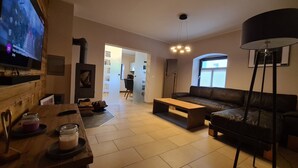 Ein modernes Wohnzimmer mit einer Couch, einem Couchtisch und einem Fernseher. Im Hintergrund sind ein Kamin, ein Essbereich und eine Küche zu sehen.