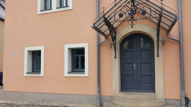Ein Gebäude mit einer dunkelblauen Tür, zwei kleinen Fenstern und einem verzierten Metallbalkon.