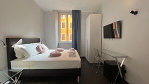 Ett modernt hotellrum med en säng, ett skrivbord, en tv och ett fönster med gardiner.