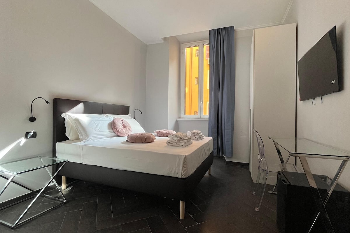 A modern hotel room with a bed, a glass desk, a flat-screen TV, and a window with curtains.