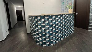 Ett receptionsområde med en receptionsdisk med ett geometriskt mönster, en krukväxt, en dörr och en vägg av glasblock.