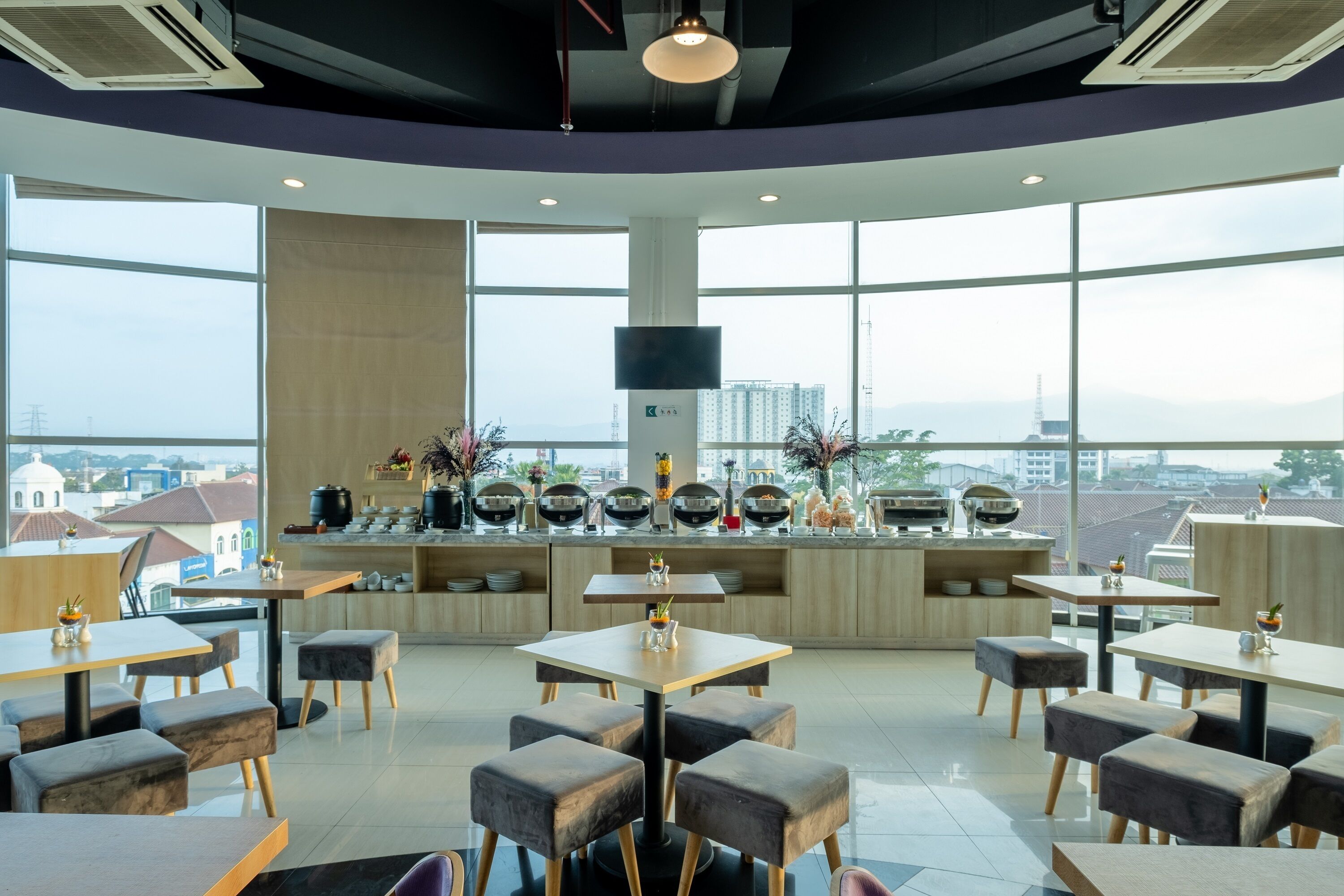 A modern restaurant with a high ceiling, large windows, and a view of the cityscape.
