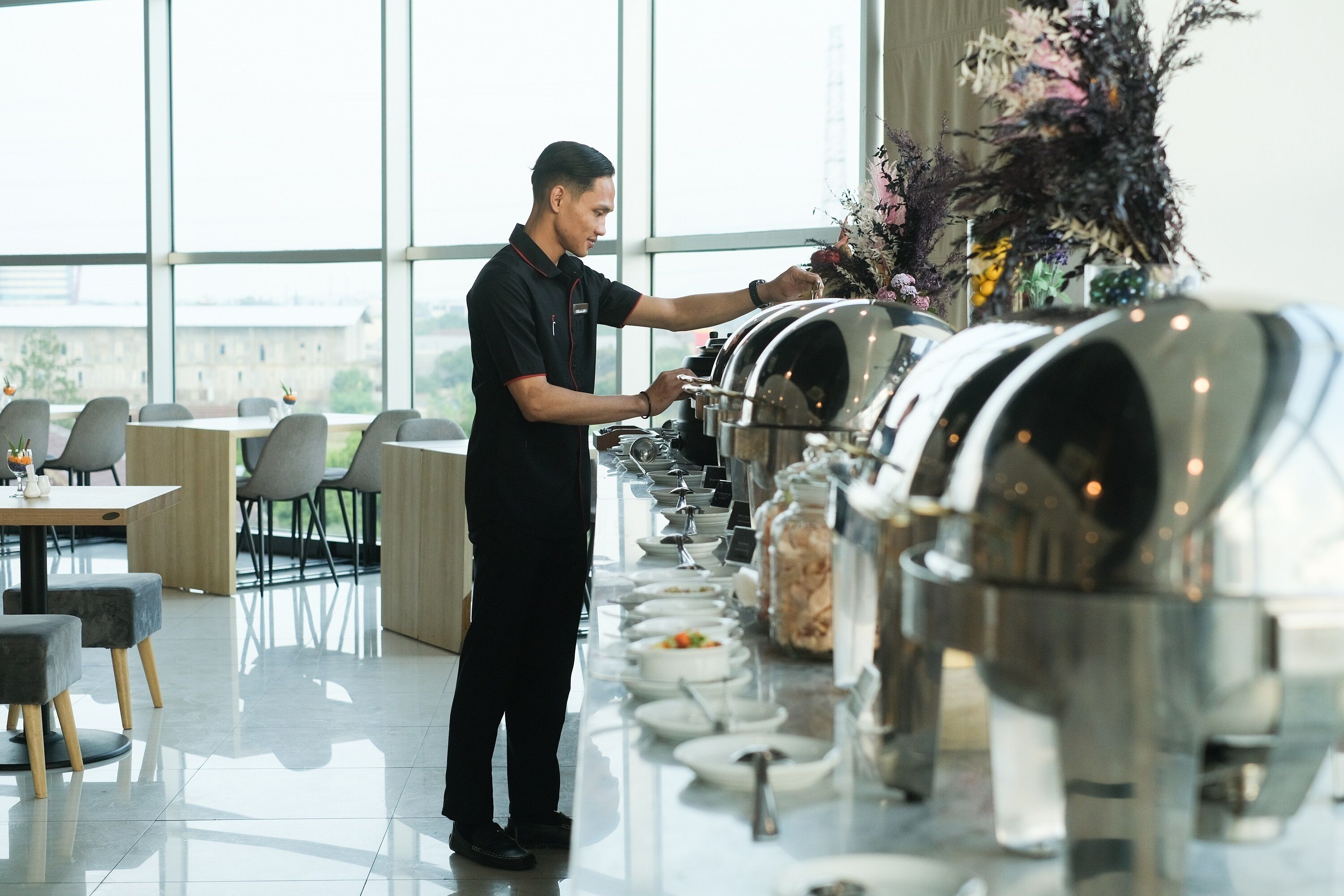 Un buffet bien garni, avec un serveur à disposition, une grande variété de plats et un intérieur moderne agrémenté de grandes fenêtres.