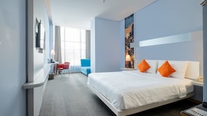 Habitación de hotel con una cama grande, un escritorio con silla, televisión y ventana con cortinas.