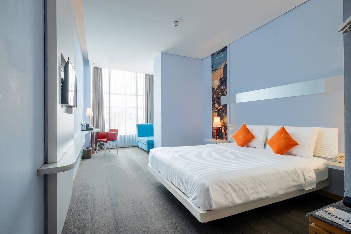 Une chambre d’hôtel avec un grand lit, un bureau avec une chaise, une télévision et une fenêtre avec des rideaux.
