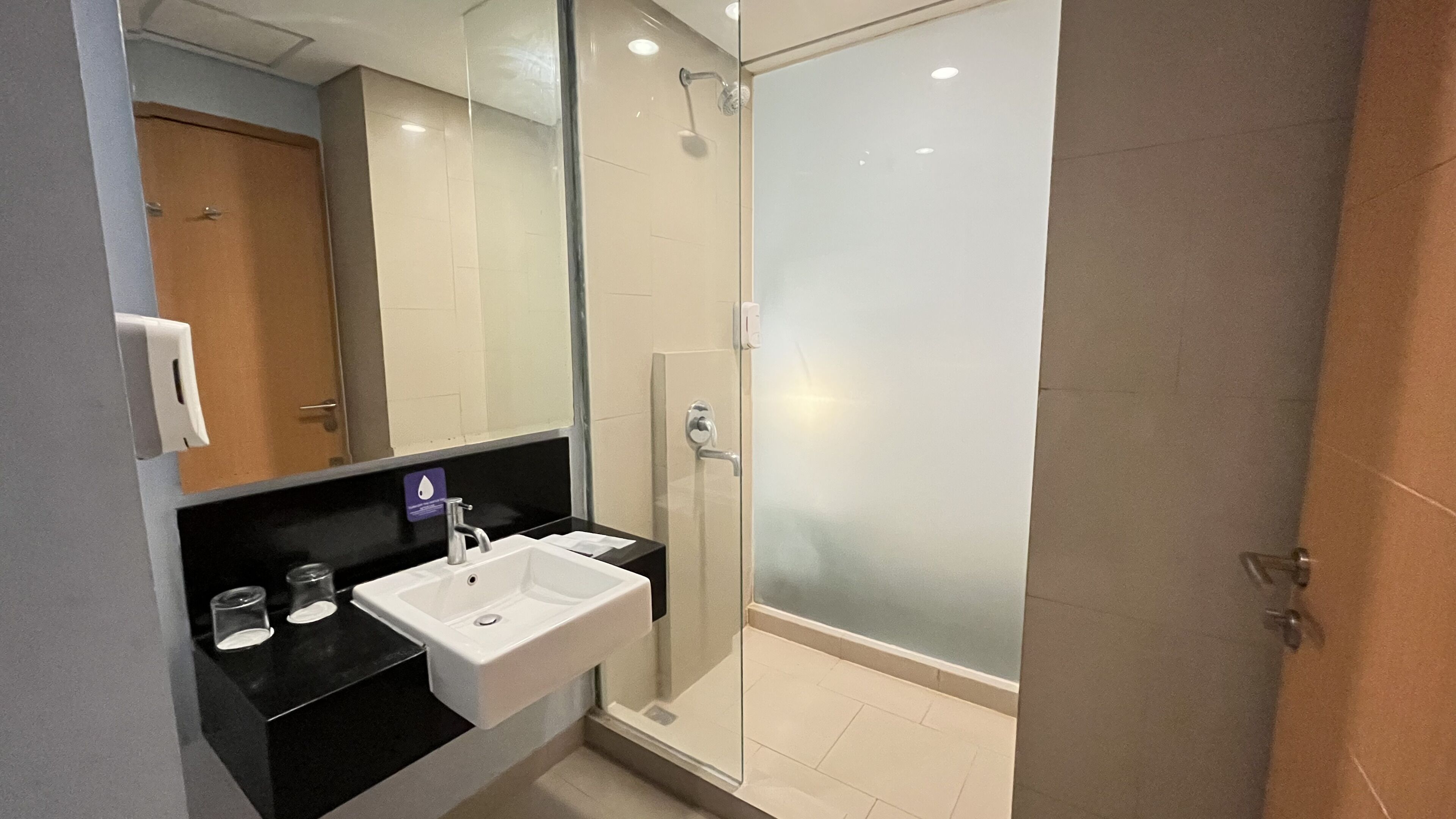 Un bagno moderno con doccia vetrata, lavandino bianco e piano di appoggio nero.