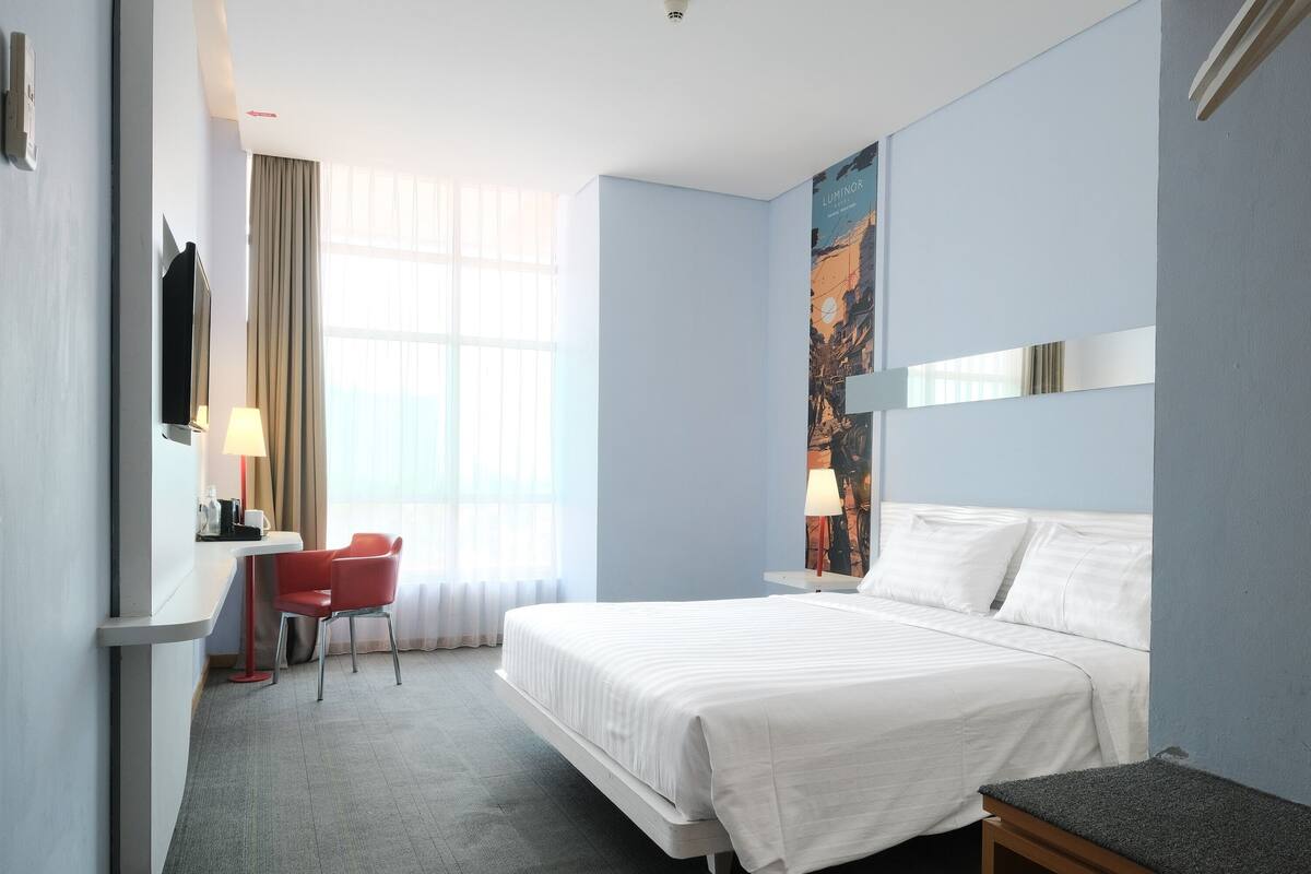 Une chambre d’hôtel avec un lit, un bureau et une chaise, une télévision et une fenêtre avec des rideaux.
