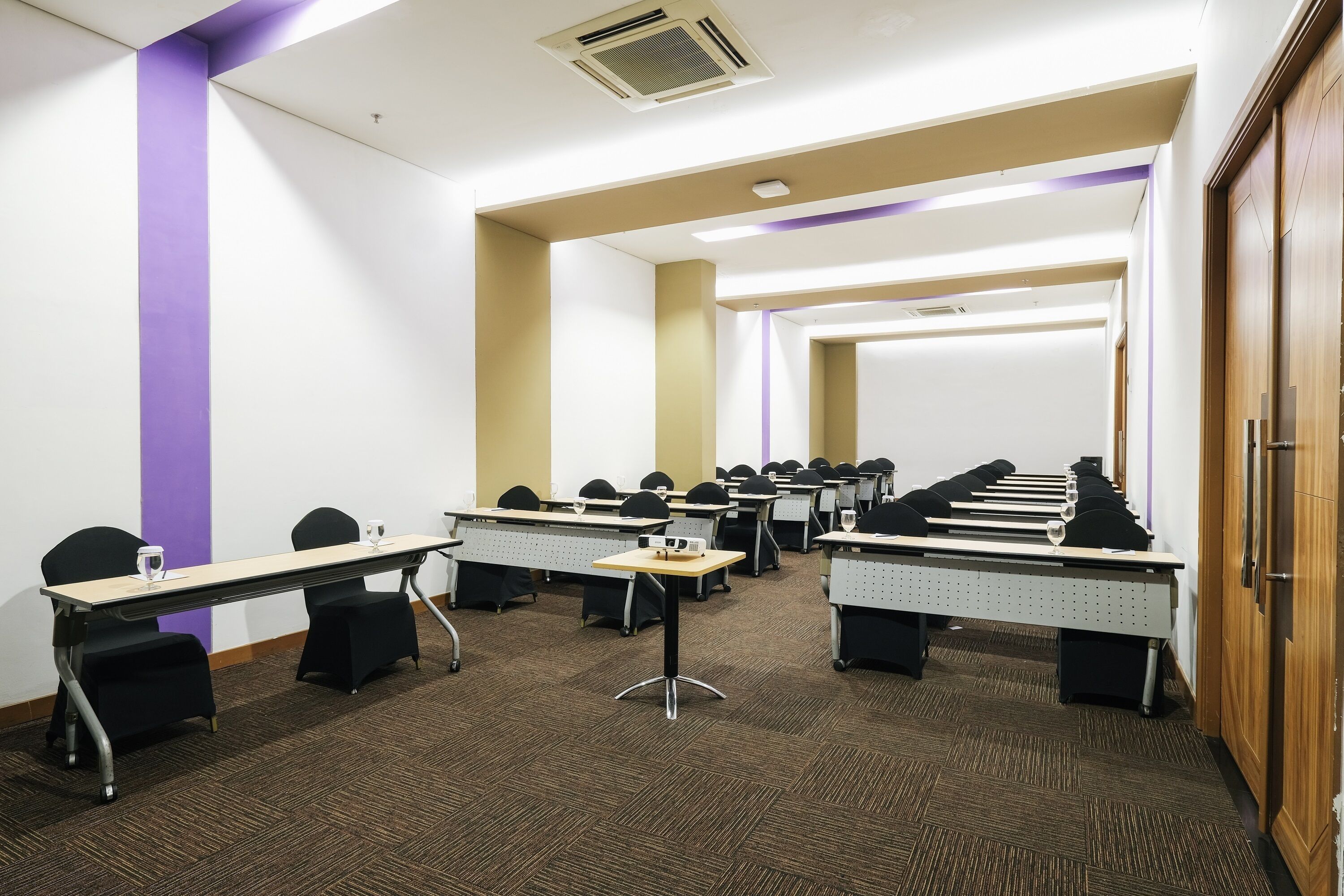 A conference room with multiple tables and chairs, carpeted floor, and a wooden door.