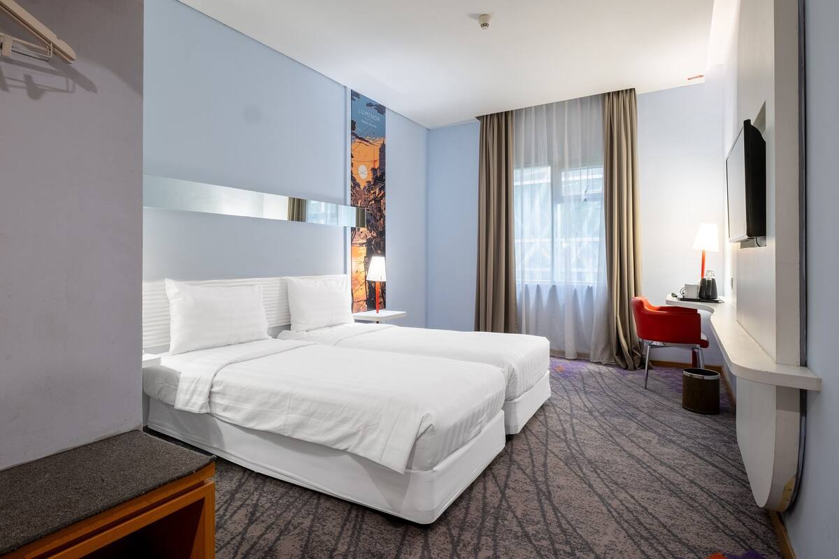 Une chambre d’hôtel avec deux lits, un bureau, une chaise, une télévision et une grande fenêtre avec des rideaux.
