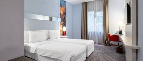 A hotel room with two beds, a desk, a chair, a TV, and a large window with curtains.