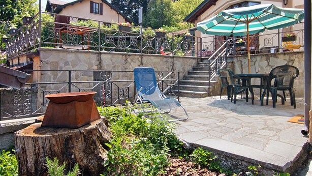 A patio area with a stone table, a chair, and a table with a striped umbrella.