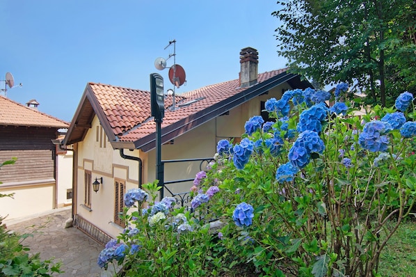 Un bâtiment doté d’un toit recouvert de tuiles, d’une antenne parabolique et d’un jardin où poussent des hortensias.