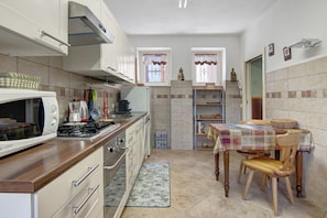 Une cuisine compacte équipée d’une cuisinière, d’un four à micro-ondes et de placards, une table à manger avec des chaises, et une petite fenêtre avec des rideaux.