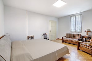 Une chambre à coucher avec un lit, une chaise en bois, un canapé et une lampe.