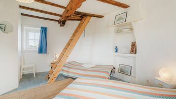 A bedroom with a sloped ceiling, wooden beams, a bunk bed, a desk, and a window with blue curtains.