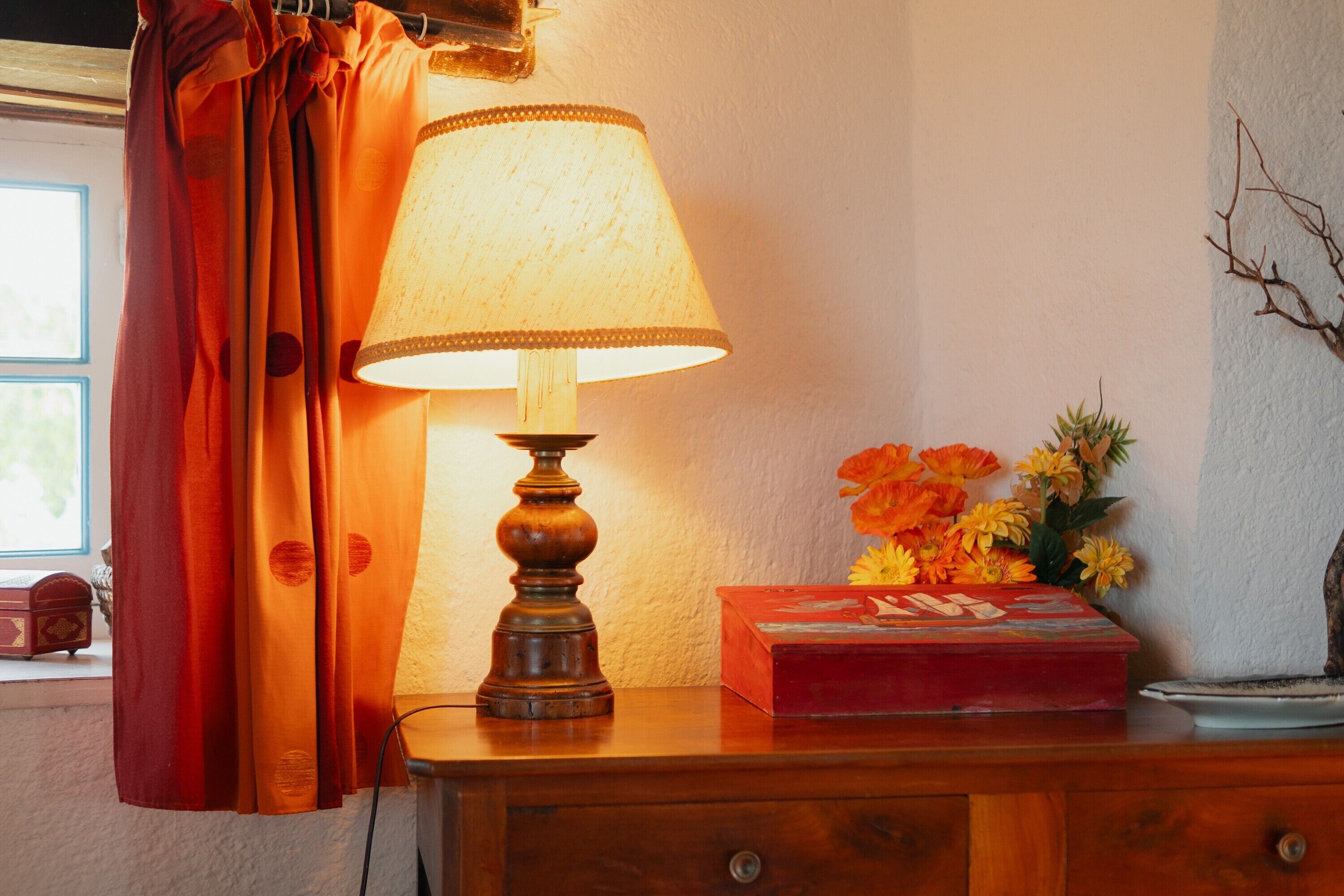 Eine Lampe auf einem Nachttisch aus Holz, eine rote Schachtel und eine Vase mit Blumen.
