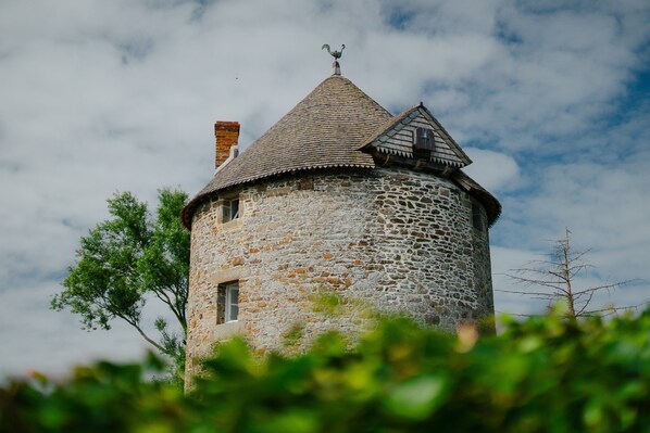 Ein steiner Turm mit einem spitz zulaufenden Dach und einer Wetterfahne.