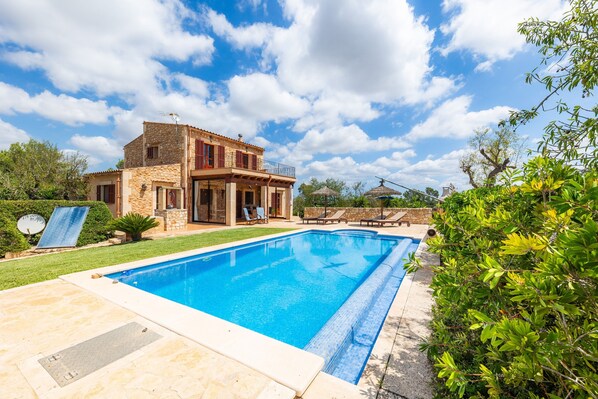 A two-story stone house with a swimming pool, a covered patio, and a garden.