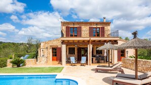 Una casa de dos pisos con piscina, mobiliario exterior y fachada de piedra.
