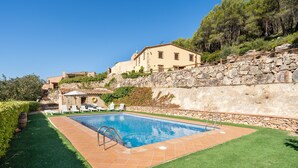 Una piscina con un muro de piedra, césped y un edificio con tejado de baldosas.