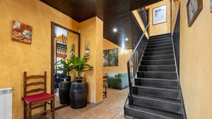 Una escalera con barandilla, una silla de madera con cojín rojo y una planta en maceta.