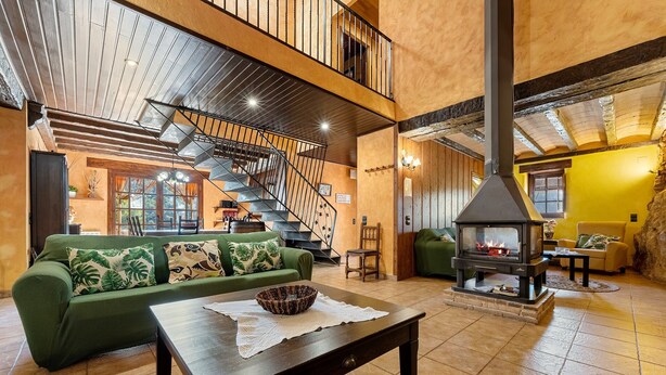Un amplio salón con un sofá verde, una mesa de centro de madera, una chimenea y una escalera.