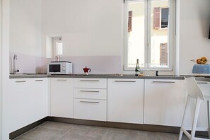 A modern kitchen with white cabinets, a microwave, and a window with shutters.