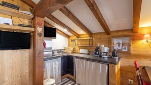A wooden interior with a kitchen area, including a sink, stove, and a television mounted on the wall. - Ski in/ski Out Holiday Apartment (Crest-Voland)