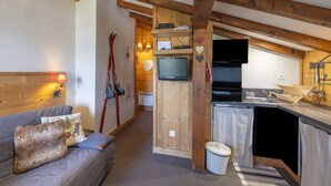 A cozy cabin interior with a sofa, a wooden ceiling, a kitchen area, and a television. - Ski in/ski Out Holiday Apartment (Crest-Voland)
