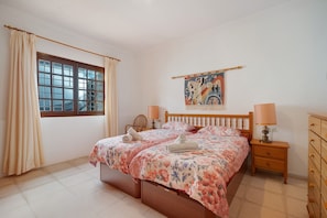 Un dormitorio con una cama, una ventana, una obra de arte colgada en la pared, una mesita de noche y un aparador.