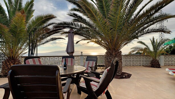 An outdoor patio with a round table and chairs, surrounded by palm trees and a view of the sea. - Vacation Home 'Biofinca Las Dulces Villa Alma' with Sea View, Pool & Wi-Fi (Guia de Isora)