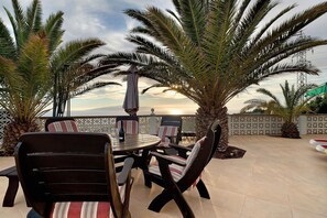 Une terrasse extérieure avec une table ronde et des chaises, entourée de palmiers et offrant une vue sur la mer.
